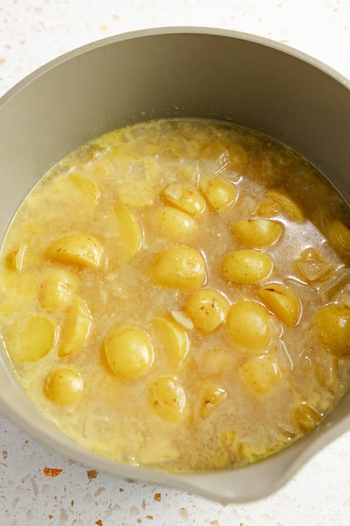 potatoes, onions, garlic, and chicken broth simmering in a pot.