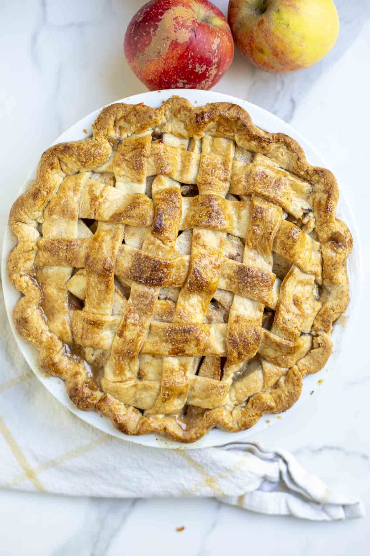 A golden brown pie on a white countertop with apples. 