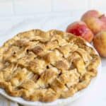 An apple pie freshly baked with three apples in the background.