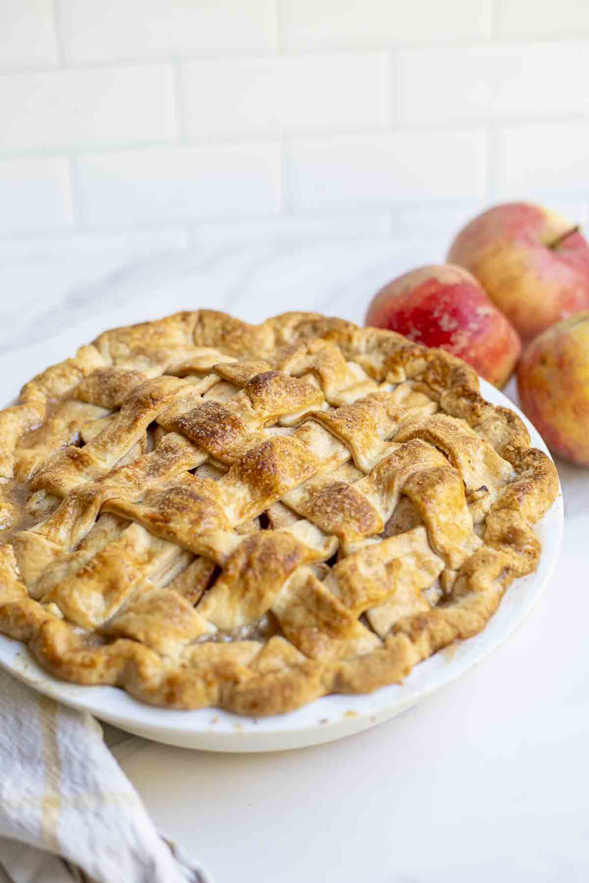 An apple pie freshly baked with three apples in the background.