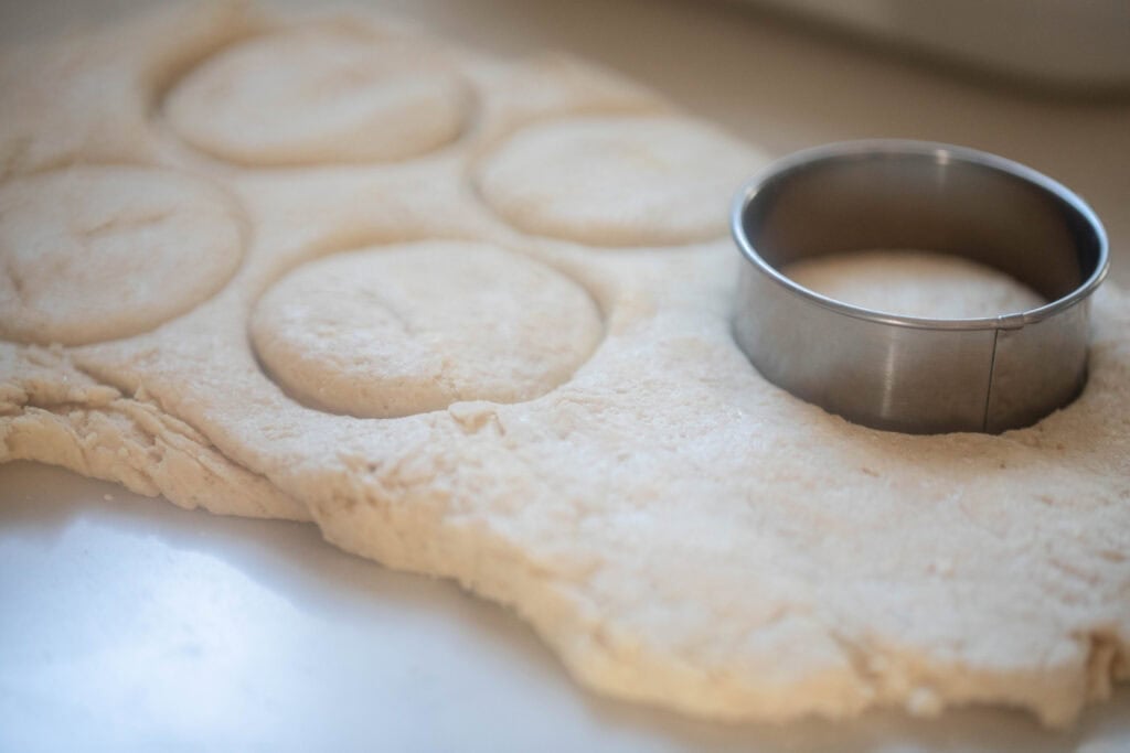 Cutting out biscuit dough on a countertop.