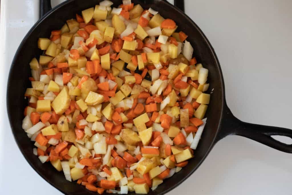 Diced carrots, potatoes, and onions in a cast iron skillet.