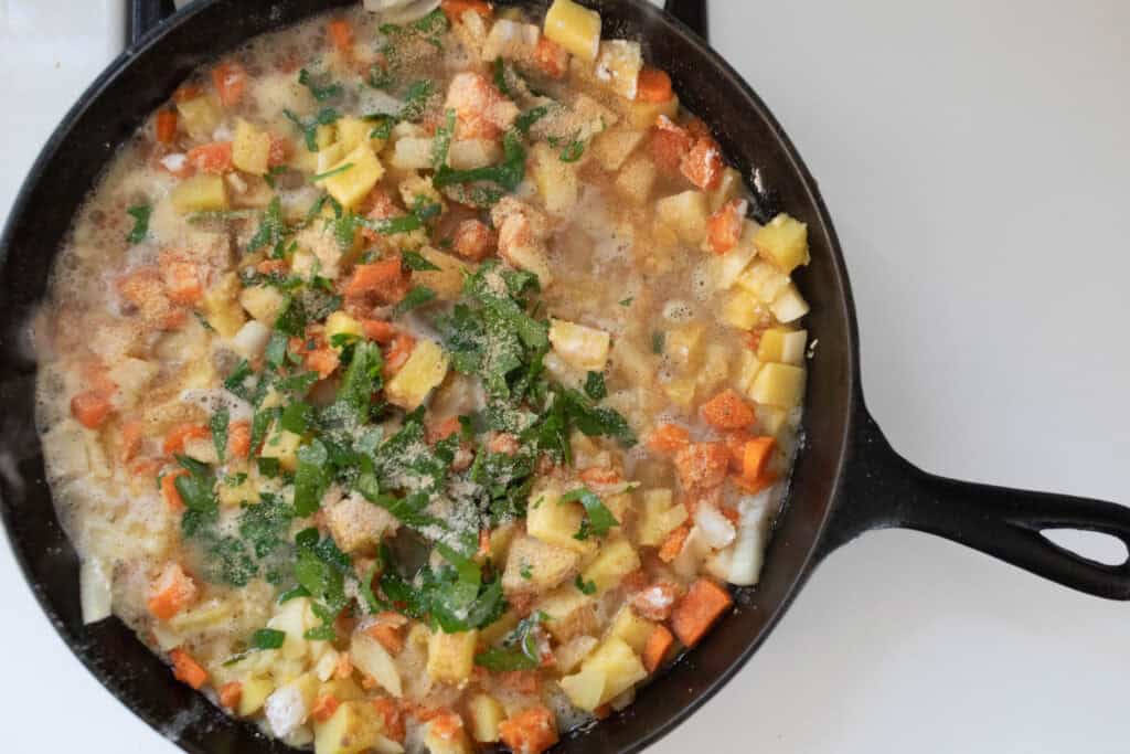 Broth and fresh parsley added to diced veggies in a cast iron skillet.