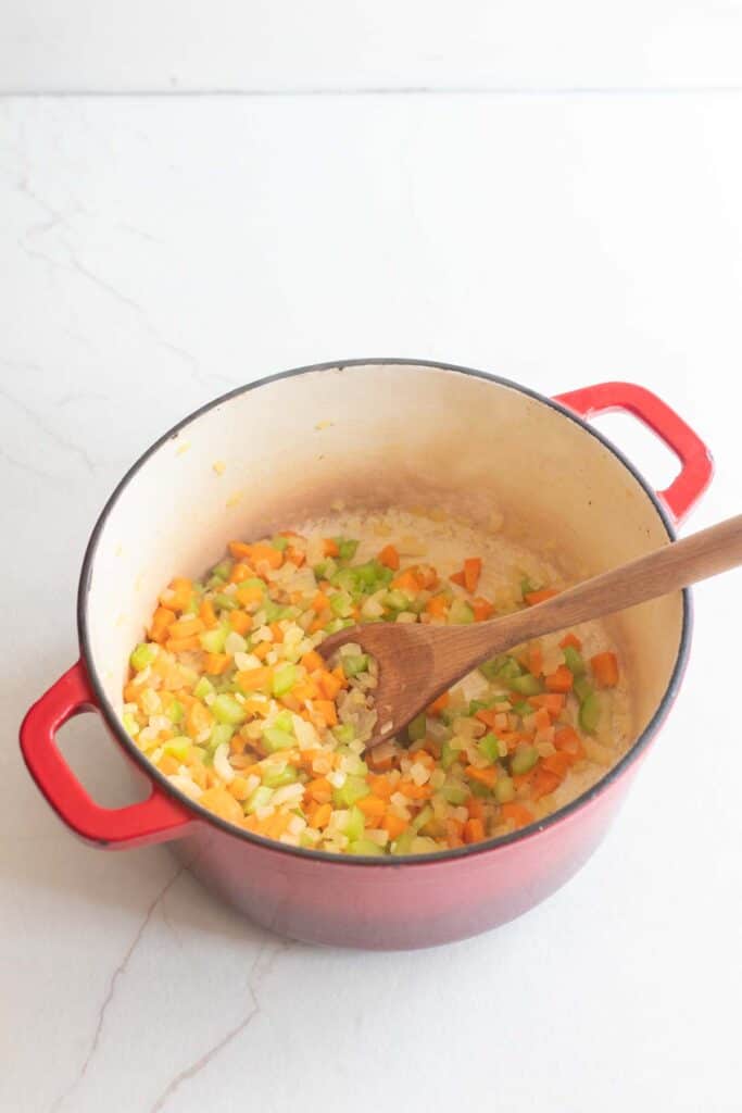 Veggies sauteing in a dutch oven with a wooden spoon.