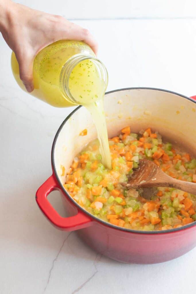 Chicken broth in a mason jar added to a dutch oven of veggies.