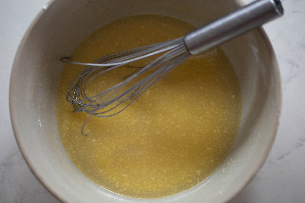 Butter, water, yeast, and honey in a bowl with a whisk.