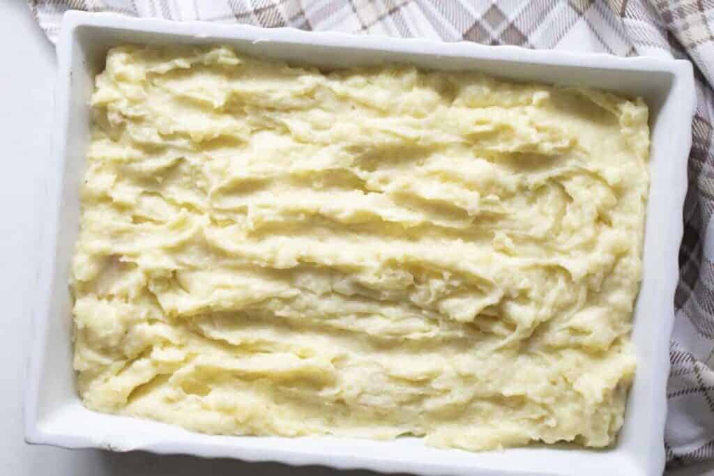 Baking dish full of garlic mashed potatoes resting on a tan and cream towel.