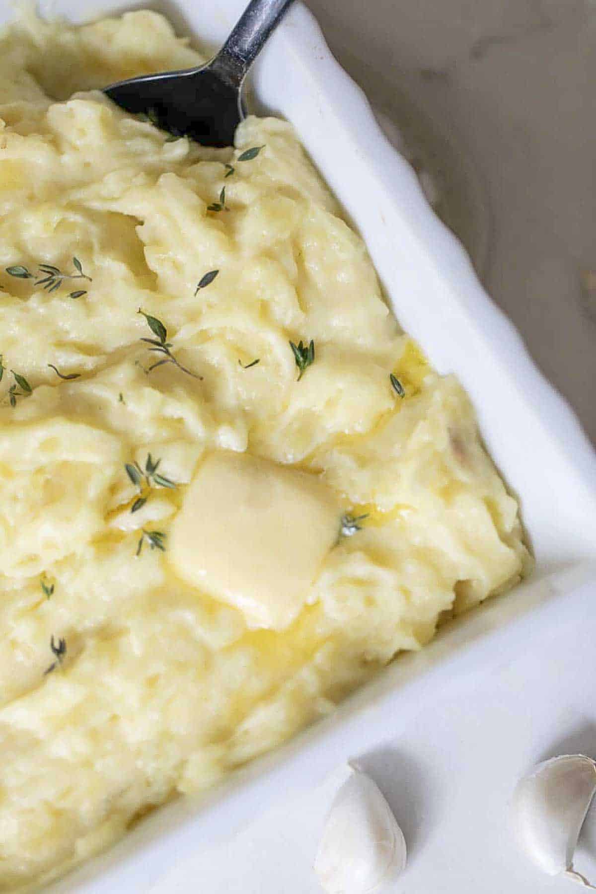 Overhead photo of garlic mashed potatoes in a dish with a spoon and herbs sprinkled on top with a pat of butter.