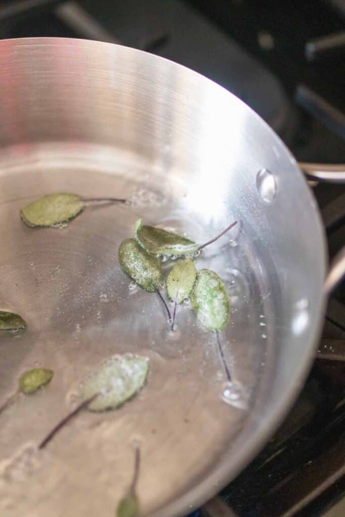 Sage leaves frying in a stainless steel pan.