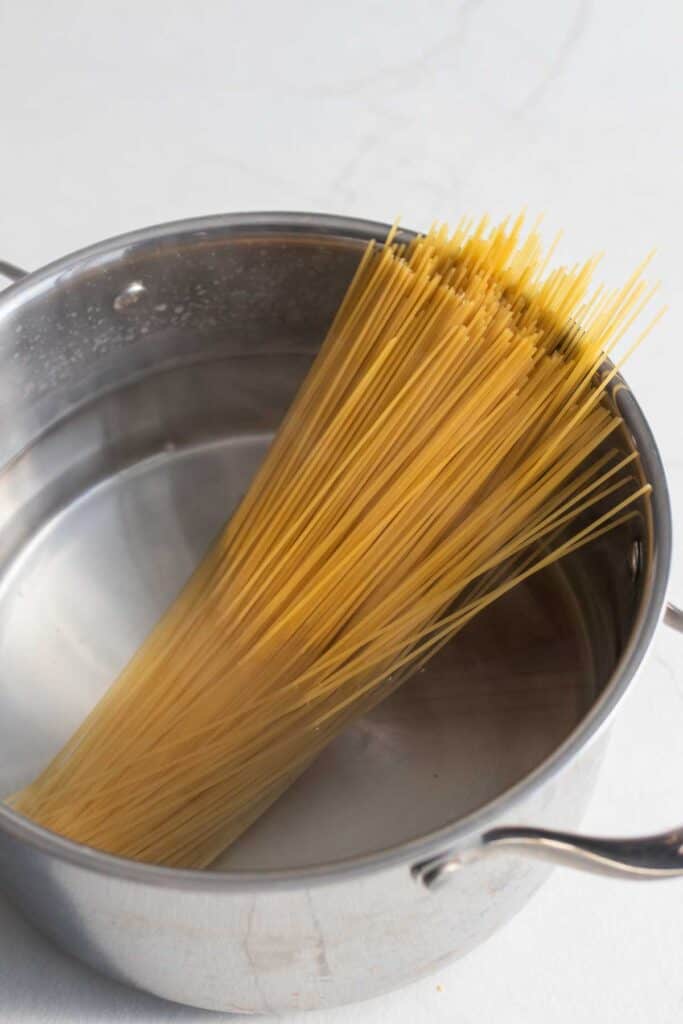 Spaghetti noodles in a stainless steel pot of water.