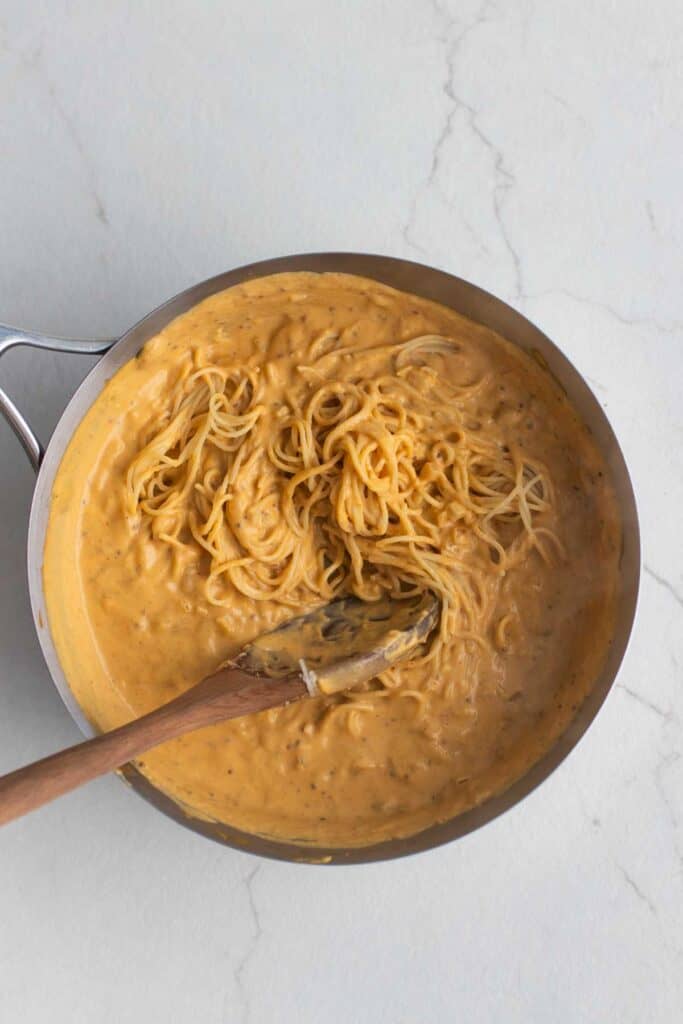 Spaghetti tossed in a pumpkin sauce with a wooden spoon in a stainless steel pan. 