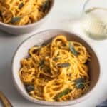 Two bowls full of spaghetti noodles covered in pumpkin pasta sauce topped with fried sage leaves.