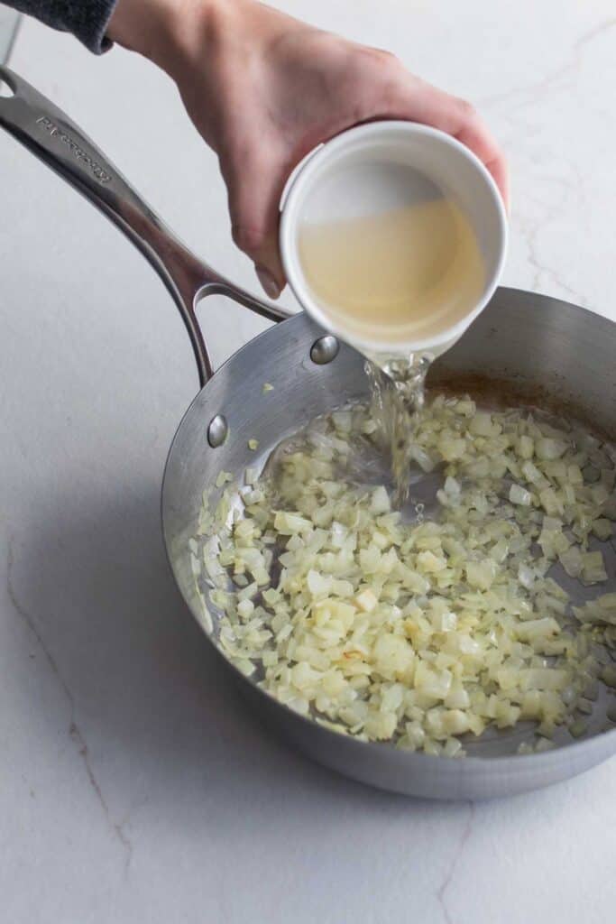 White wine added to a stainless steel pan of cooked diced onions.