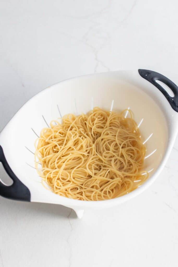 Spaghetti noodles draining in a white strainer.