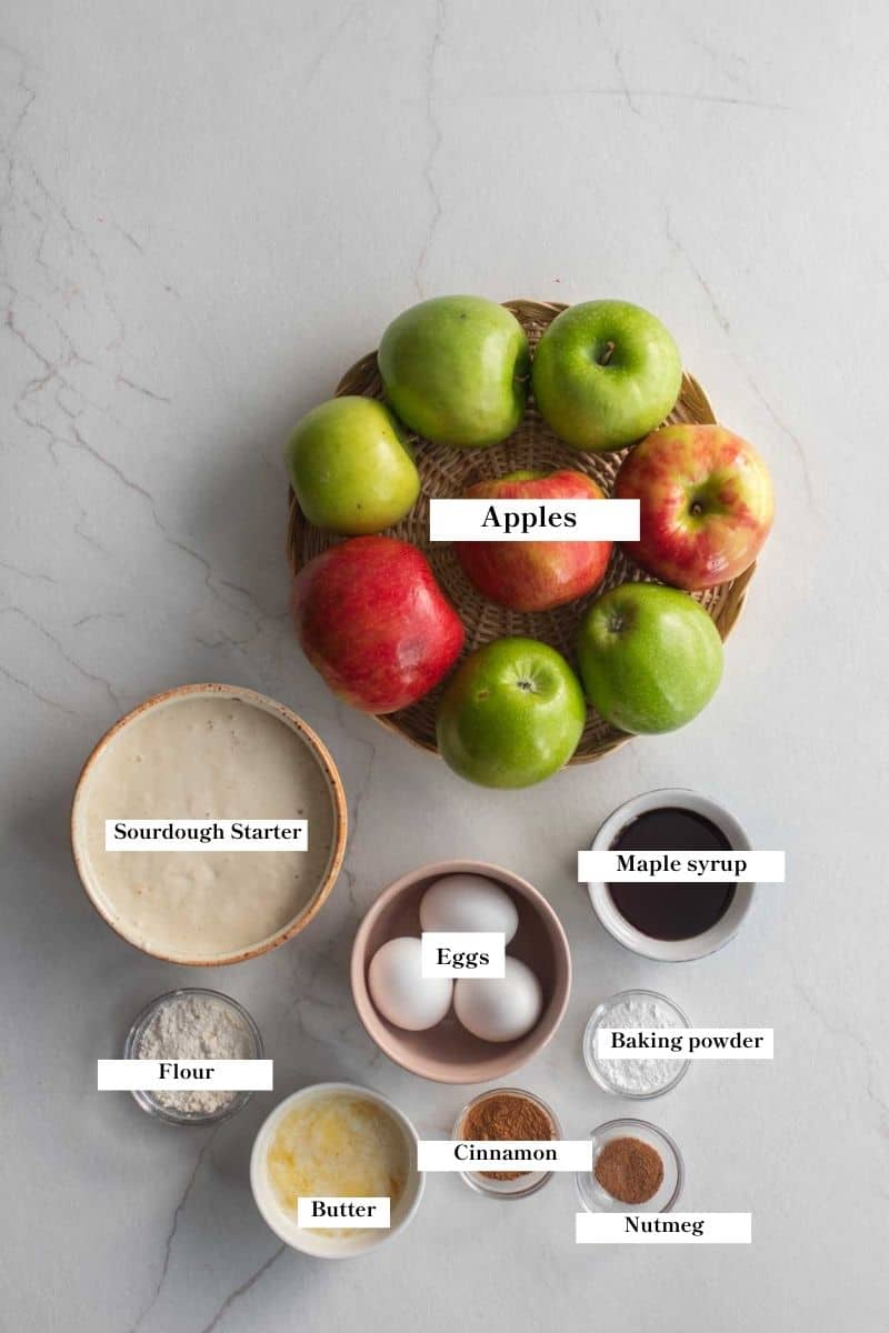 Apples in a bowl next to small bowls of all the ingredients to make apple cobbler on a countertop. 