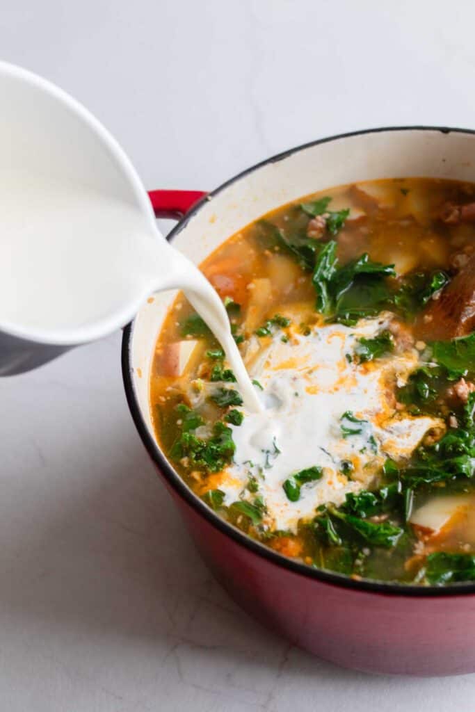 Cream being poured into a dutch oven full of soup.