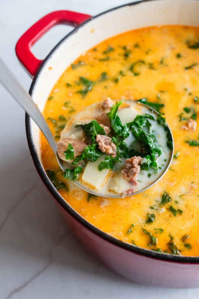 A ladle scooping out soup from a dutch oven.