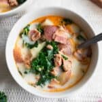 A bowl of zuppa toscana soup with a spoon sticking out.