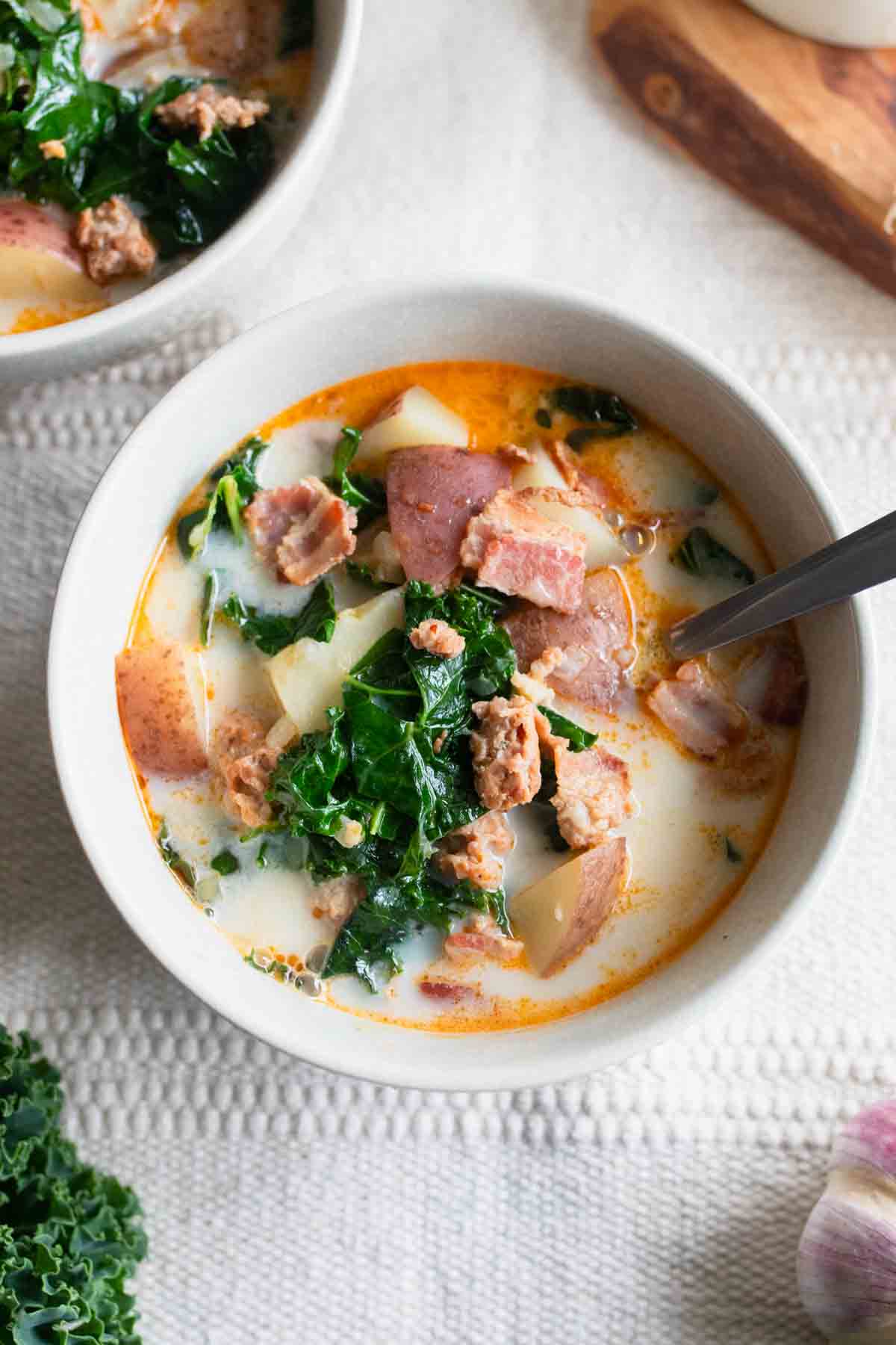 A bowl of zuppa toscana soup with a spoon sticking out.