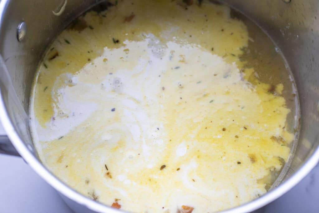 Cream added to chicken and gnocchi soup in a large pot.