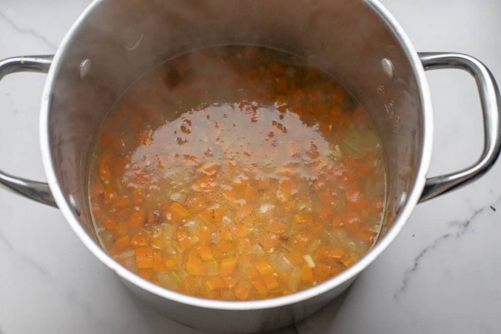 Broth added to a large stock pot of cooked diced veggies. 