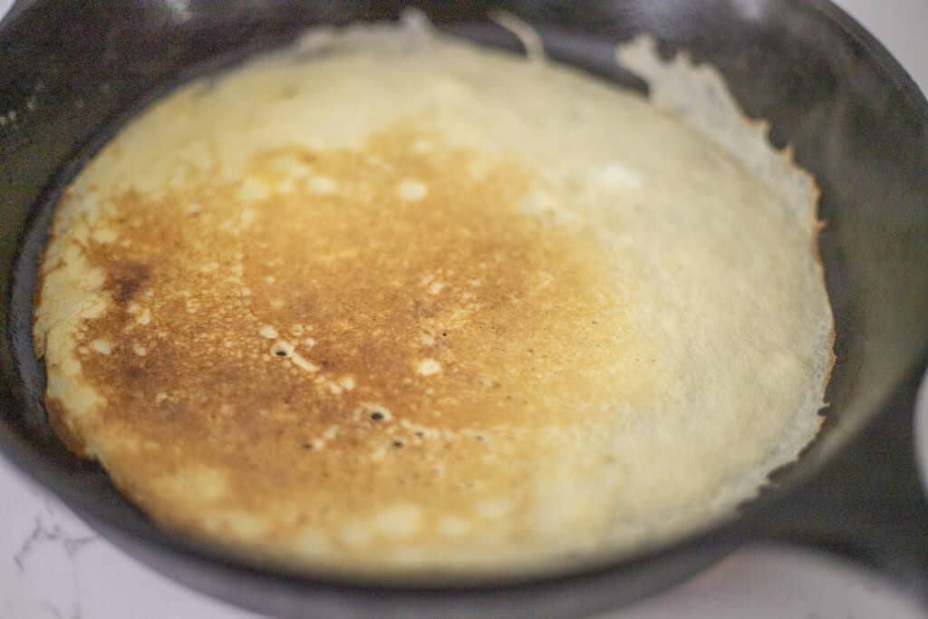 Sourdough crepe cooked on one side in a cast iron skillet.