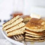 A stack of pancakes on a plate cut with a fork.