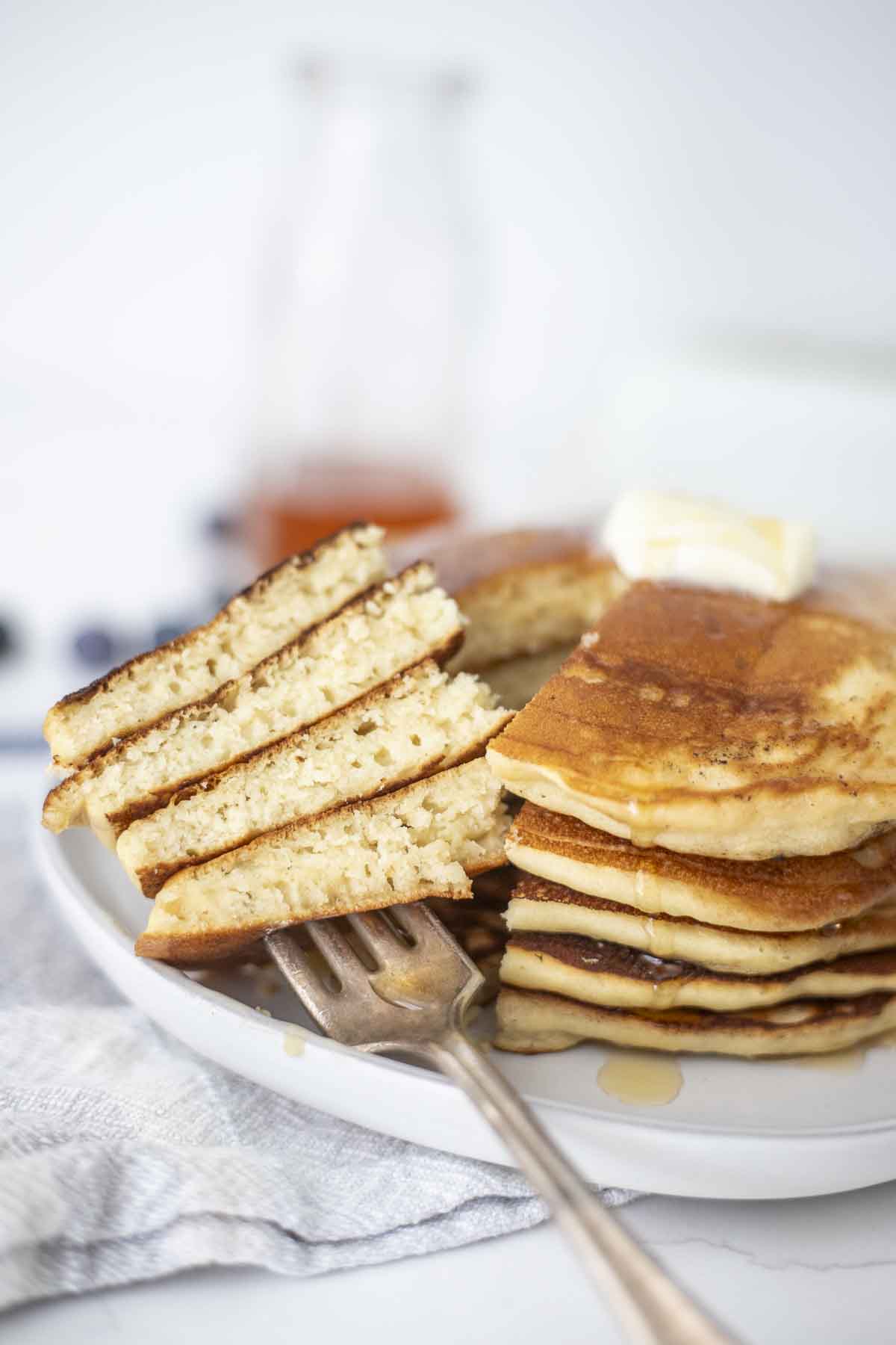 A stack of pancakes on a plate cut with a fork. 