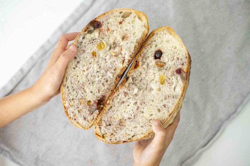 Hands holding two halves of sourdough fruit bread.