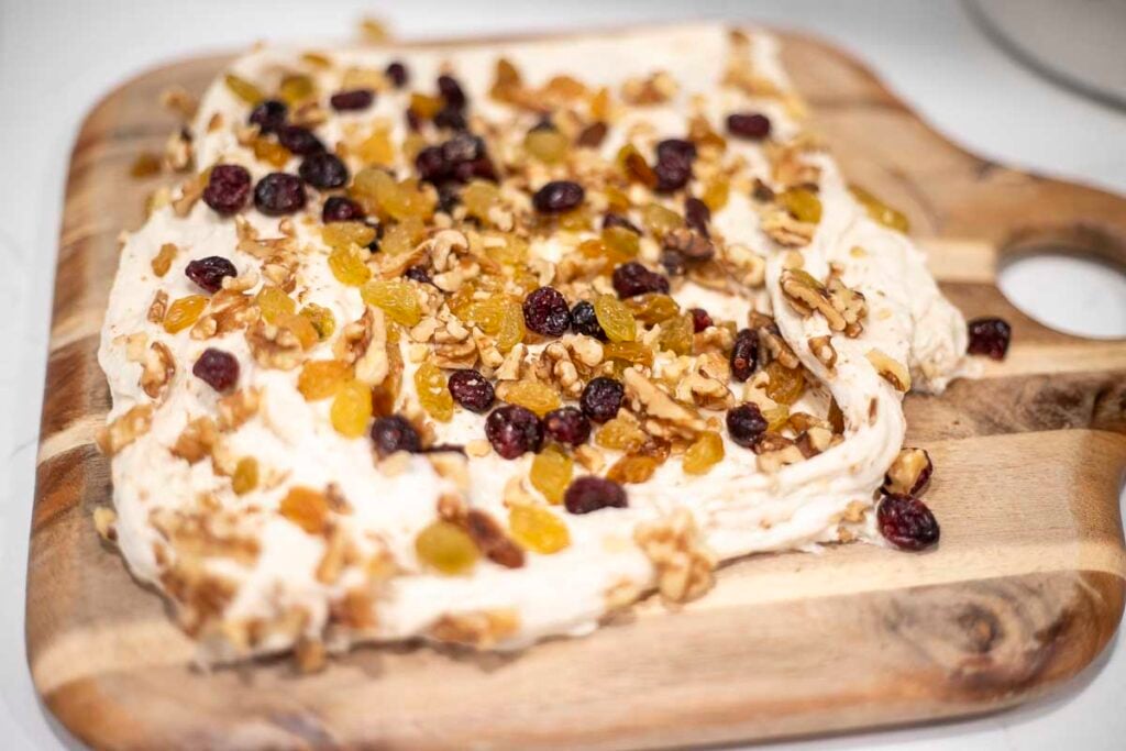 Dough on a cutting board with fruit and nuts added to it.