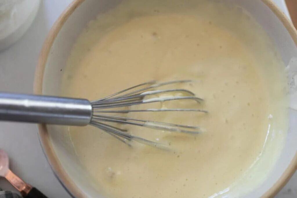 A whisk in a bowl of well mixed waffle batter, with baking soda added.