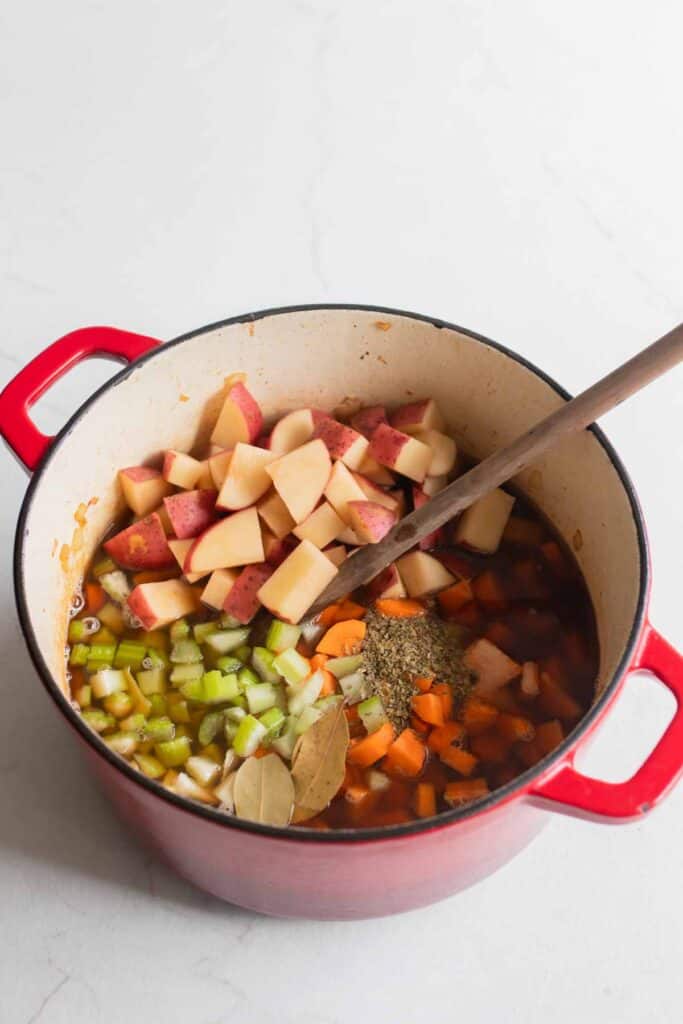 Potatoes, carrots, celery, and herbs added to the Dutch oven.