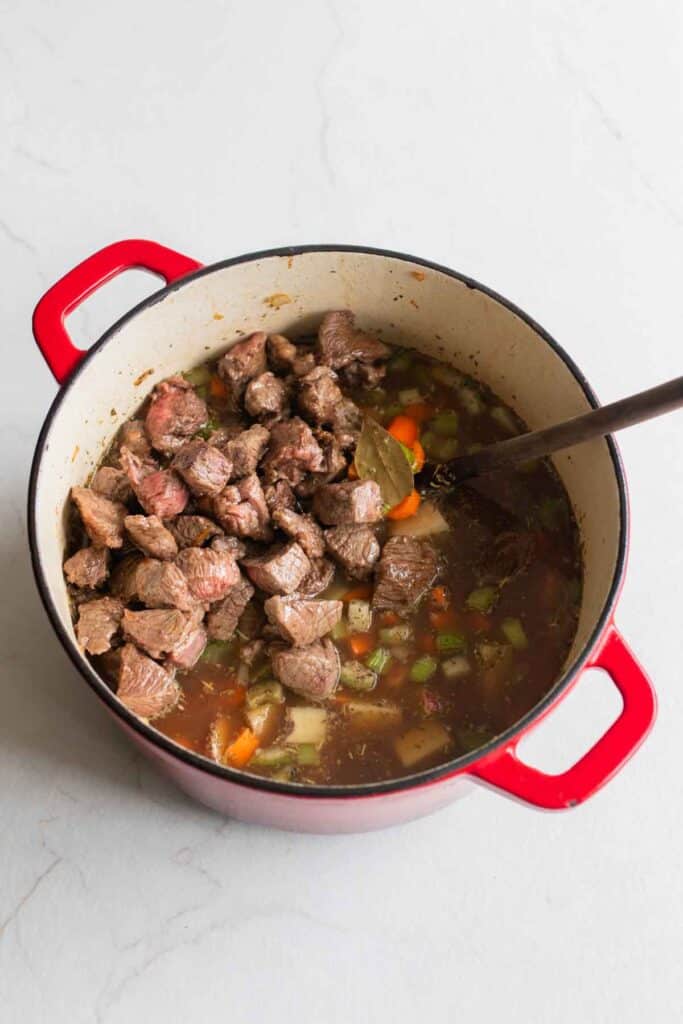 A Dutch oven full of beef stew with a large spoon sticking out.