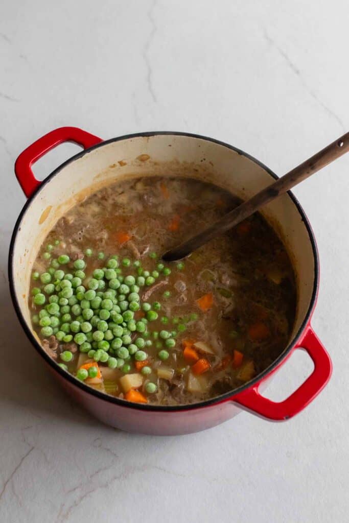 Frozen peas added to beef stew in a Dutch oven.