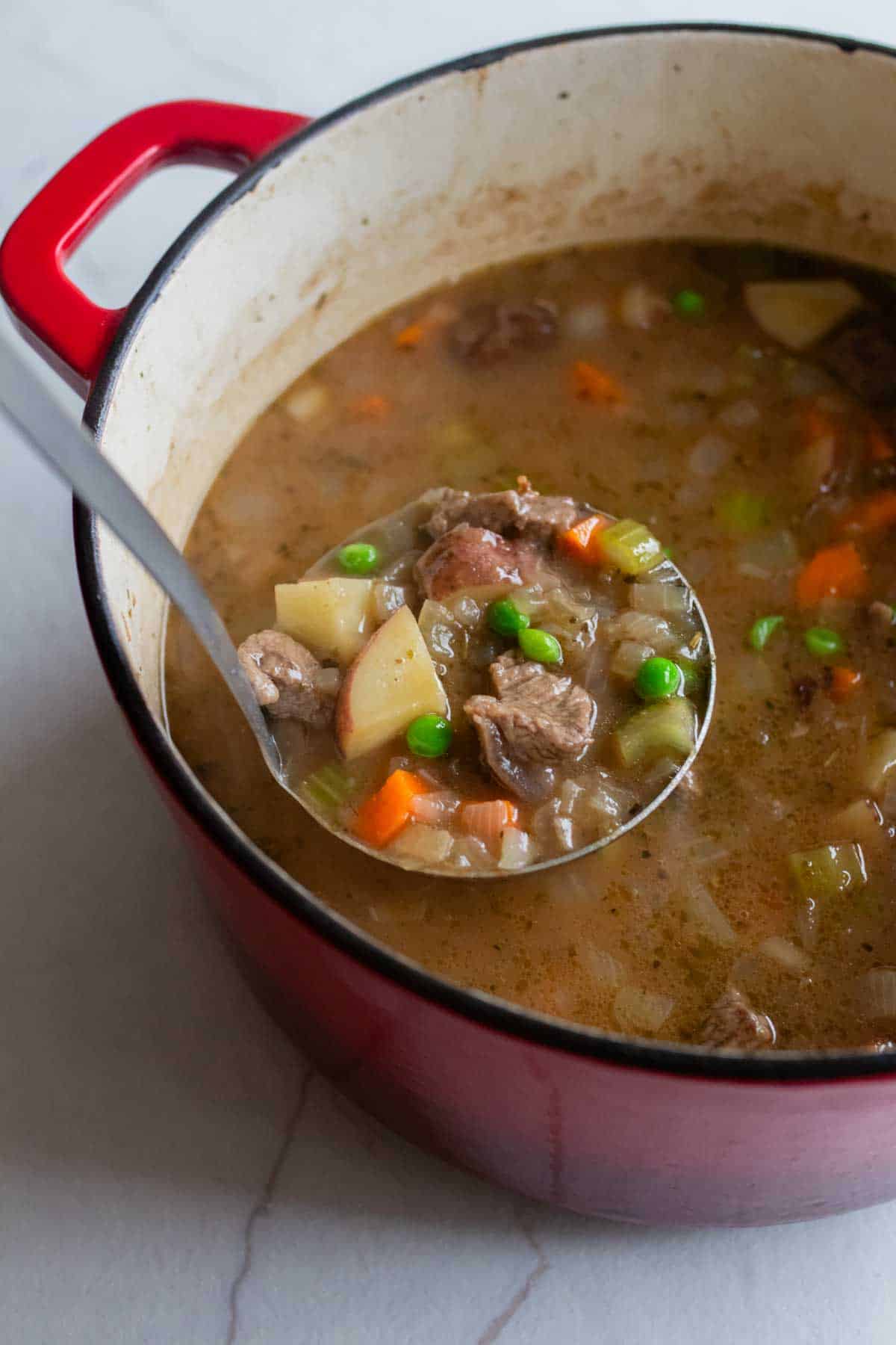 A ladle removing beef stew from the Dutch oven. 