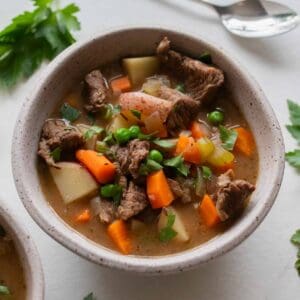 A bowl of beef stew with a silver spoon laying on the counter next to it.