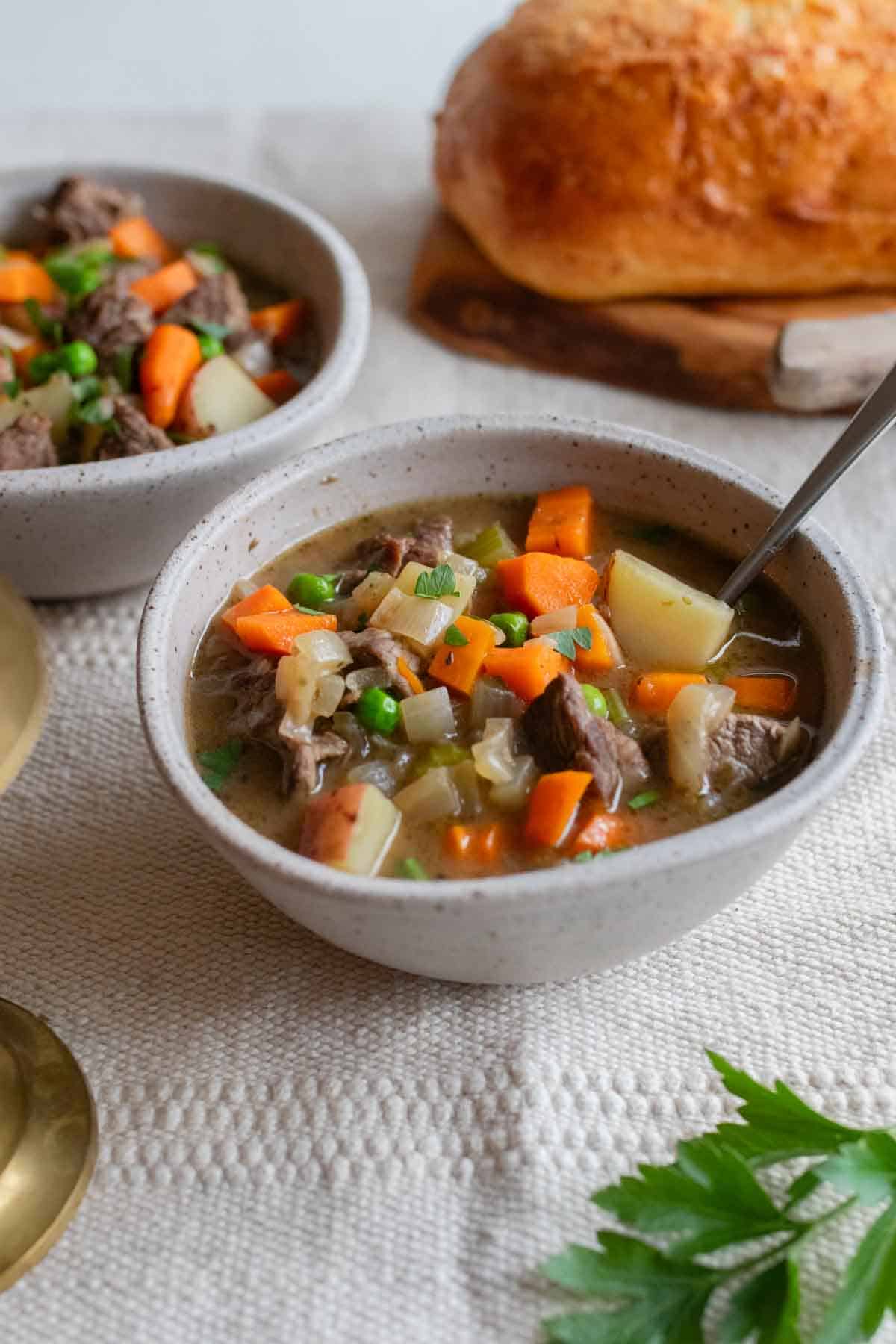 Bowls of beef stew with a loaf of bread in the background. 