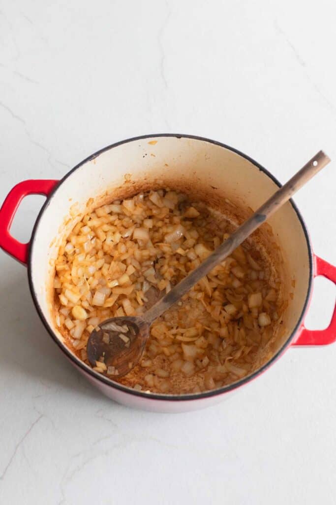 Onion cooking in a Dutch oven with a wooden spoon. 