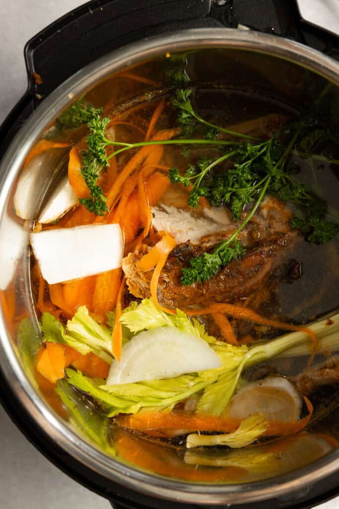 Veggie scraps and chicken bones covered in water in an instant pot.