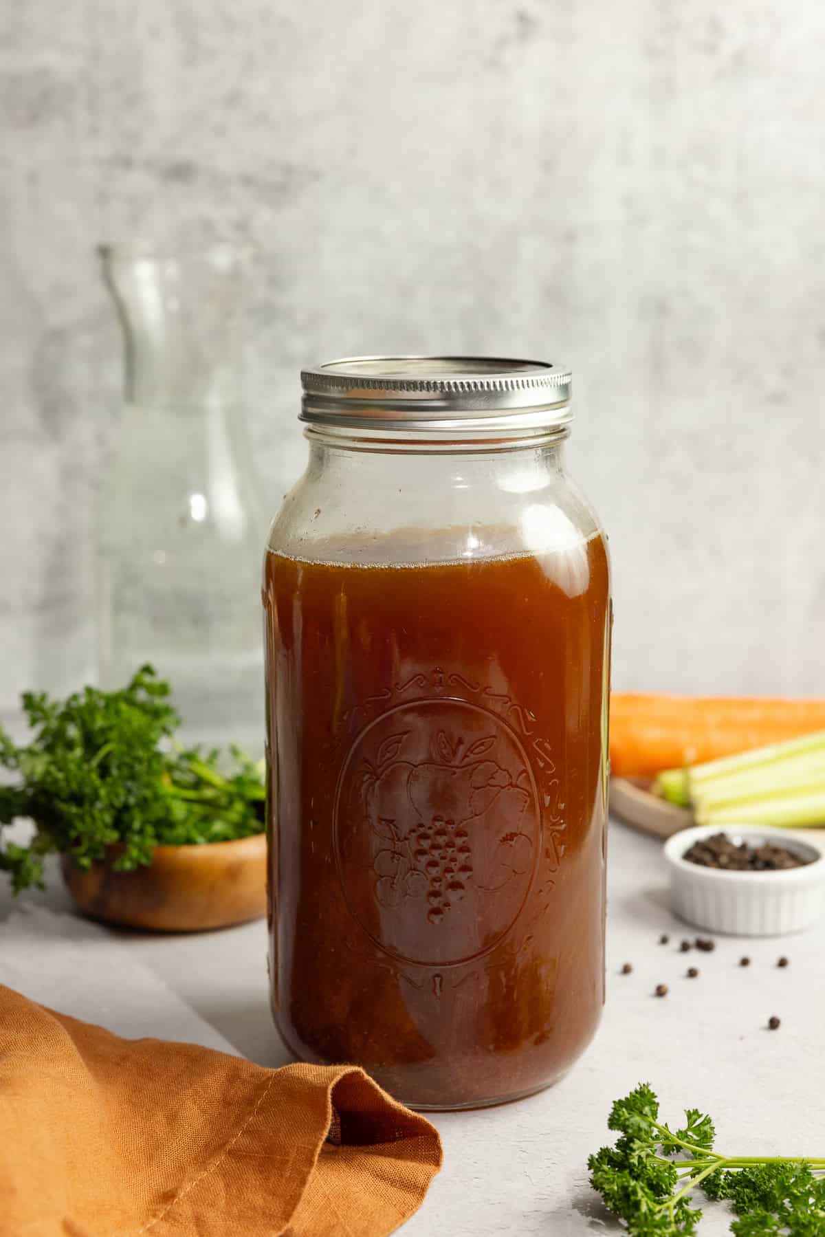 Bone broth in a half gallon mason jar surrounded by ingredients.