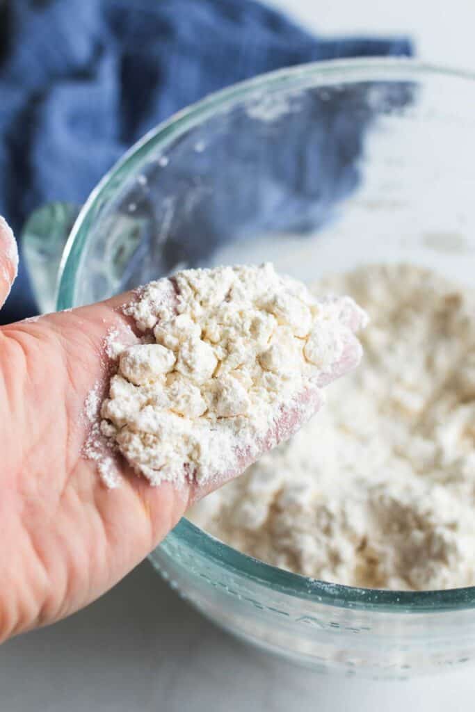 A hand holding the flour and butter mixture to show how the butter should be pea sized.