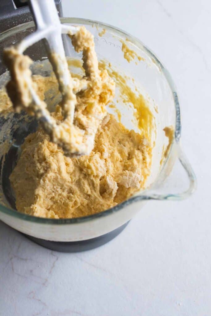 A paddle attachment lifted out of a stand mixer bowl that has wet and dry ingredients mixed together.