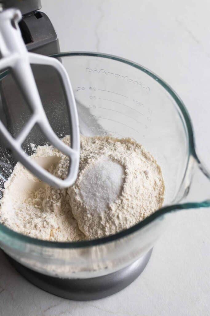 Flour and other dry ingredients in a clear stand mixer bowl. 