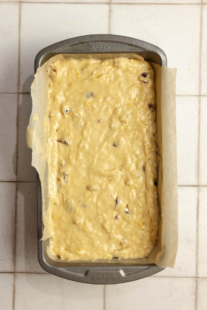 Banana cranberry bread batter in a parchment paper lined loaf pan.