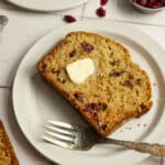 A slice of banana bread on a white plate with a fork.