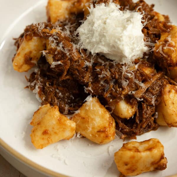 A plate full of cooked gnocchi topped with a meat sauce and cheese.