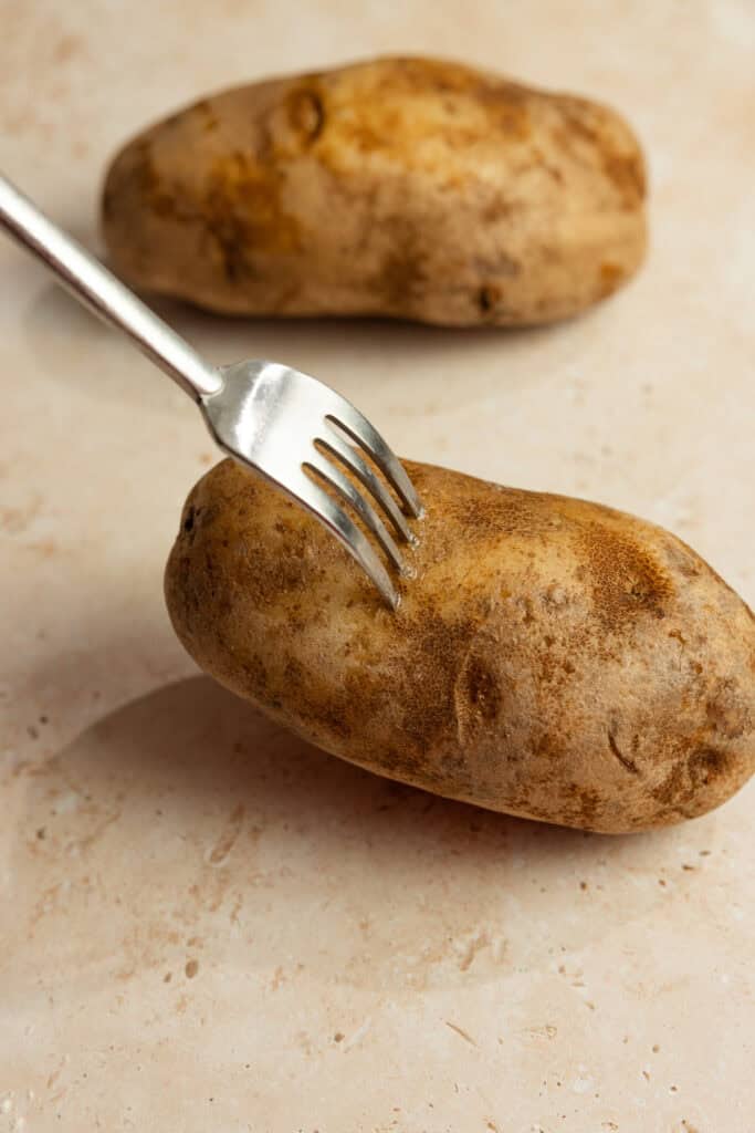 Two potatoes with skin on, with a fork sticking out of one.