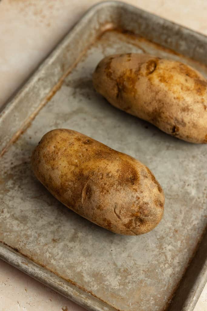 Two potatoes on a baking sheet.