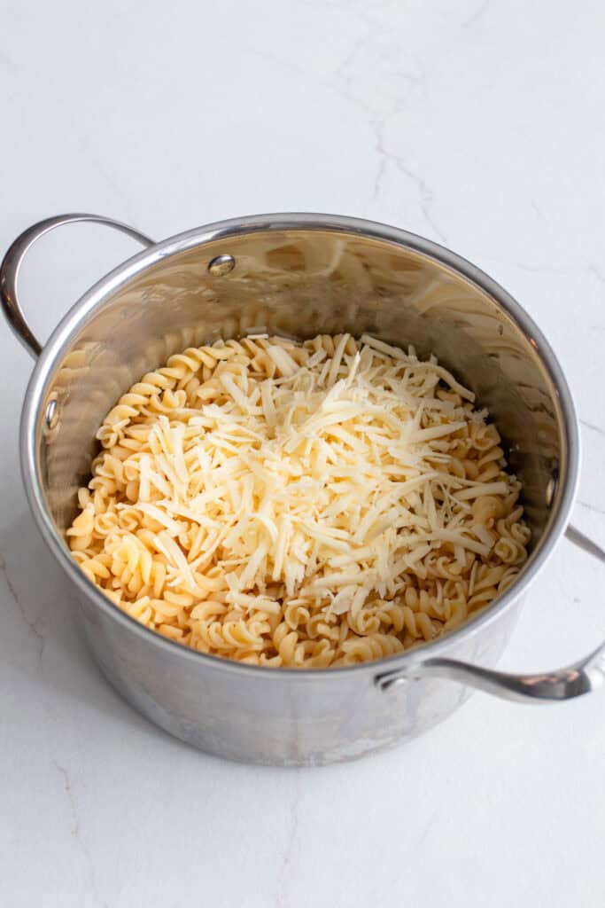 Noodles in a large pot with shredded cheese on top.