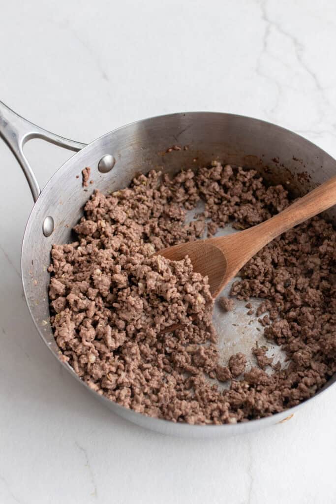 Ground beef browned in a skillet with a wooden spoon.